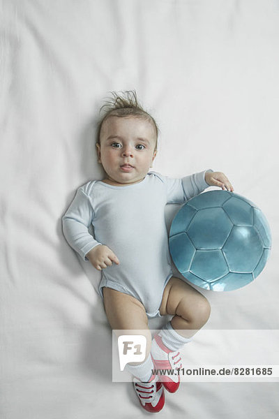 Ein kleiner Junge in Baby-Fußballschuhen neben einem Fußball