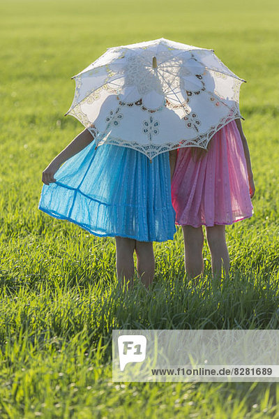 Zwillingsschwestern stehen auf einem sonnigen Feld unter einem Schirm