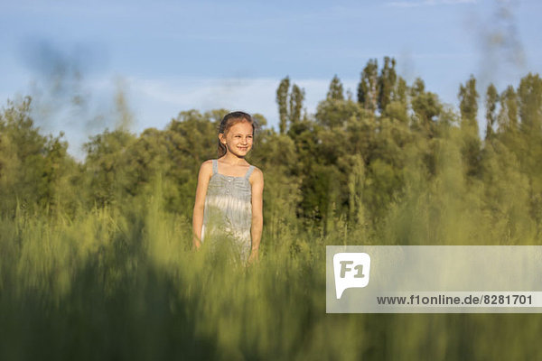 Ein junges  fröhliches Mädchen steht auf einem Feld und schaut auf die Aussicht.