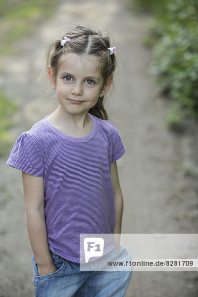 Ein junges lächelndes Mädchen  das auf einem Feldweg steht.
