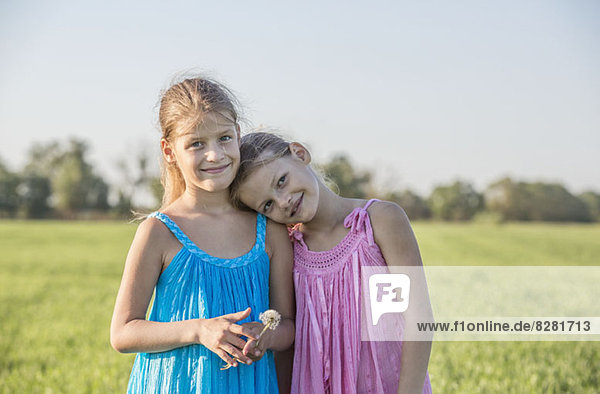 Liebevolle Zwillingsschwestern auf einem sonnigen Feld stehend