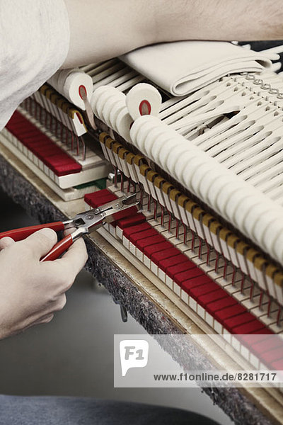 Ein Klaviermechaniker  der mit einer Zange ein Klavier repariert.