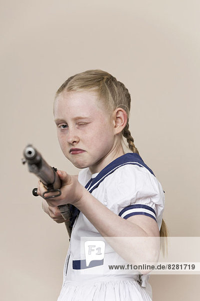 Ein hartes Mädchen  das ein Matrosenkleid trägt und ein Gewehr auf die Kamera richtet.