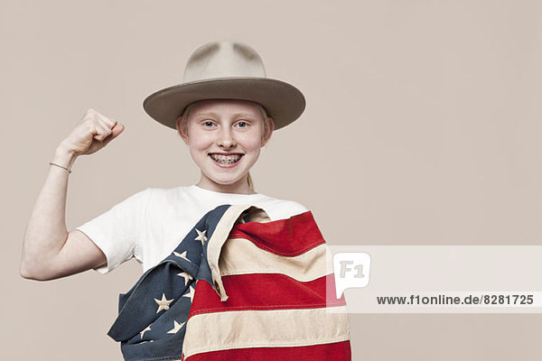 Ein lächelndes Mädchen mit einem Rangerhut  der in eine amerikanische Flagge gehüllt ist und eine Faust macht.