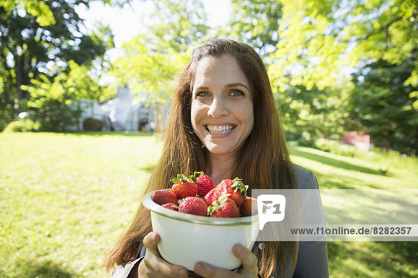 Auf der Farm. Eine Frau trägt eine Schale mit frisch gepflückten Bio-Erdbeeren.