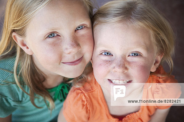 A Portrait Of Two Sisters Smiling. Two Young Girls  With Blue Eyes And Blonde Hair.