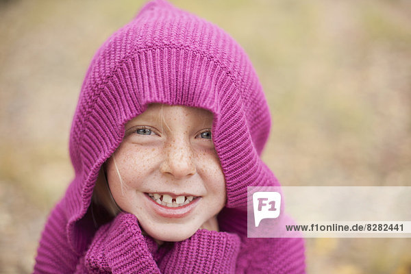 Ein Mädchen in einem magentafarbenen Kapuzenpullover,  die Kapuze bedeckt ihren Kopf