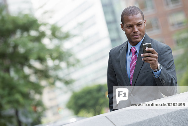Ein junger Mann in einem Business-Anzug mit blauem Hemd und roter Krawatte. Auf einer Straße in New York City. Mit einem Smartphone.