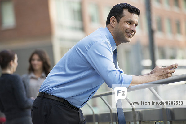Geschäftsleute im Freien. Ein lateinamerikanischer Geschäftsmann in Hemd und Krawatte  angelehnt an einem Geländer. Entspannend.