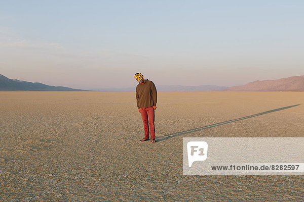 Die Landschaft der Schwarzen Felsenwüste in Nevada. Ein Mann  der eine Tiermaske trägt. Wirft einen langen Schatten auf den Boden.
