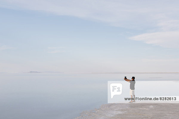 A Man Standing At Edge Of The Flooded Bonneville Salt Flats At Dusk  Taking A Photograph With A Tablet Device  Near Wendover.