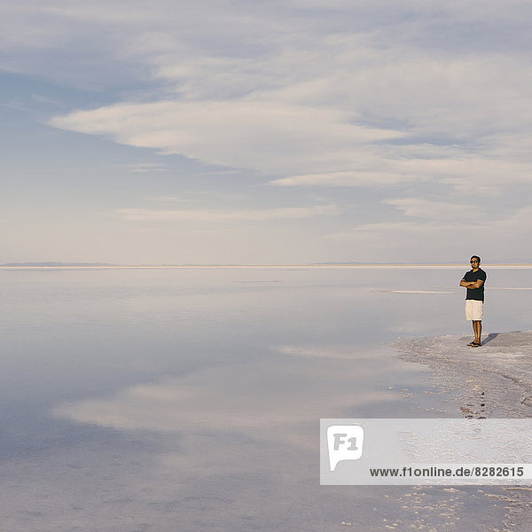 A Man Standing At Edge Of The Flooded Bonneville Salt Flats At Dusk. Arms Folded.