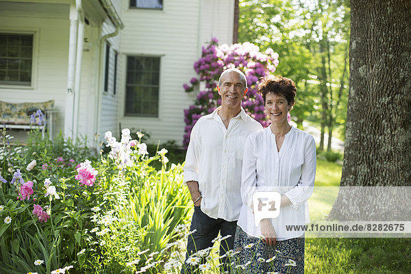 Organic Farm. Summer Party. A Mature Couple In White Shirts Standing Together Among The Flowers.