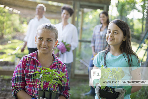 Biologische Landwirtschaft. Sommerfest. Zwei Mädchen sitzen mit jungen Pflanzen  ein reifes Paar und eine junge Frau schauen zu.