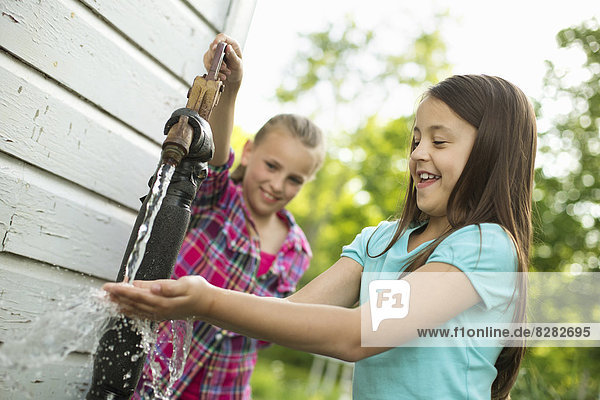 Organic Farm. Two Girls Washing Their Hands Under The Flow Of Water From A Pump In The Yard.