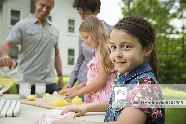 A Summer Family Gathering At A Farm. A Girl Slicing And Juicing Lemons To Make Lemonade.