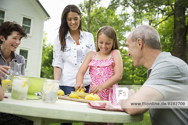 Eine Sommer-Familienzusammenkunft auf einem Bauernhof. Ein Mädchen schneidet Zitronen in Scheiben und entsaftet sie zu Limonade.