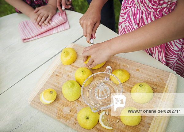 Eine Sommer-Familienzusammenkunft auf einem Bauernhof. Ein Schneidebrett auf dem Tisch. Ein Kind zerschneidet Zitronen und entsaftet sie für Limonade.