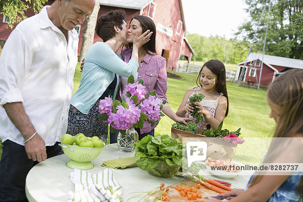 Familienfeier. Ein gedeckter Tisch mit Salaten und frischem Obst und Gemüse. Eltern und Kinder. Eine Mutter  die eine Tochter auf die Wange küsst.