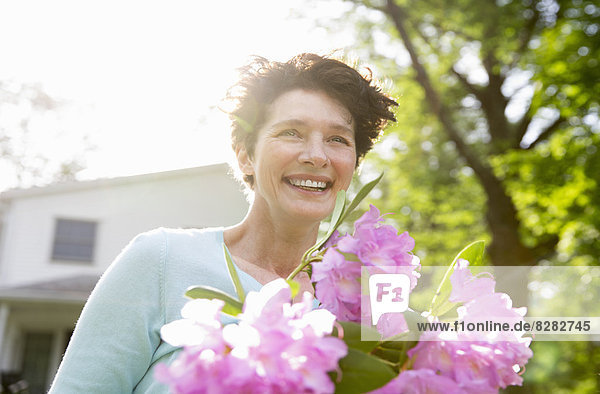 Familienfeier. Eine Frau  die einen großen Strauß Rhododendronblumen trägt und breit lächelt.