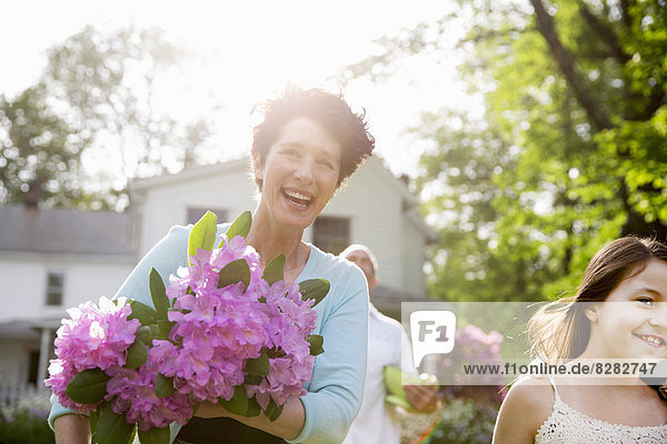Family Party. A Woman Carrying A Large Bunch Of Rhododendron Flowers  Smiling Broadly.