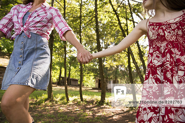 Eine Frau und ein junges Mädchen halten sich an den Händen und laufen unter den Bäumen entlang.