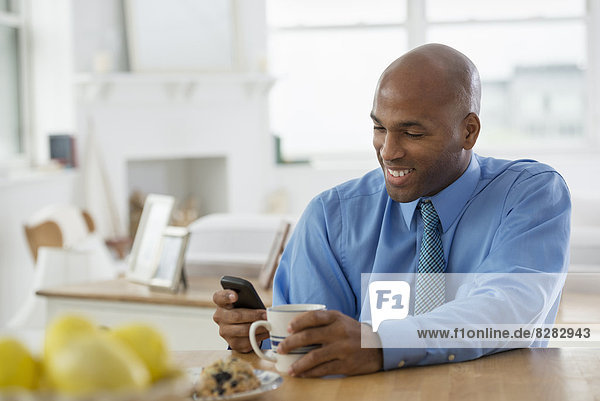 Ein Mann in einem blauen Hemd  der mit einem Smartphone an einer Frühstücksbar sitzt.