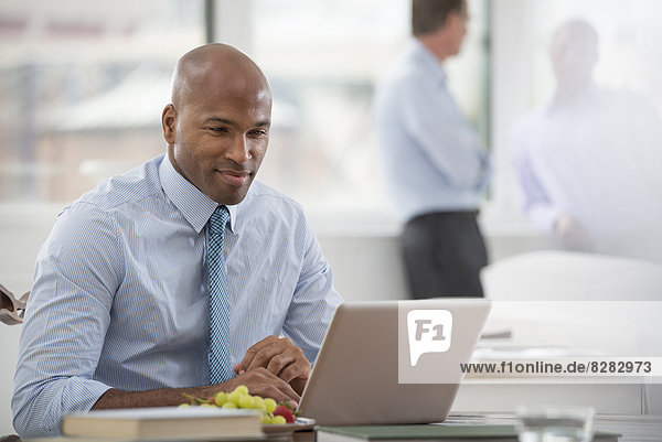 Büroleben. Ein Geschäftsmann in Hemd und Krawatte  der an einem Schreibtisch sitzt und einen Laptop-Computer benutzt.