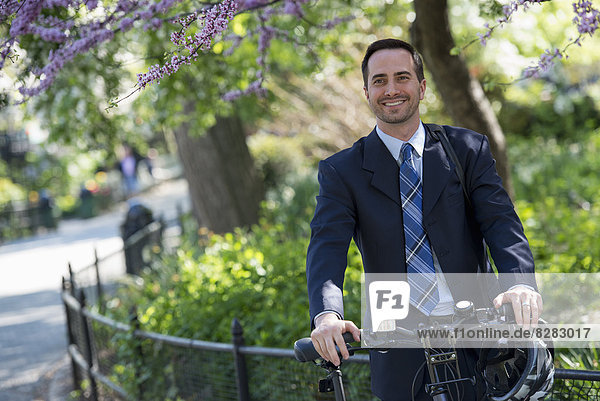 Ein Mann in einem Business-Anzug rittlings auf einem Fahrrad mit einem Helm in der Hand.
