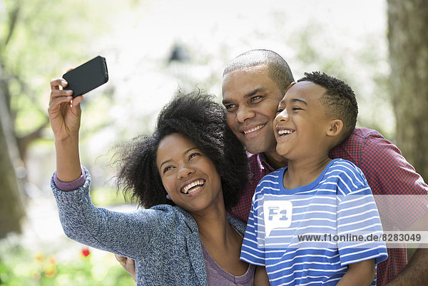 Zwei Erwachsene und ein junger Junge fotografieren mit einem Smartphone.