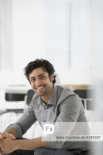 Business. A Man Seated With His Hands Clasped In A Relaxed Pose. Smiling And Leaning Forwards.