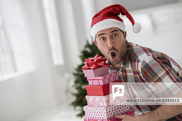 Innenministerium. Wir feiern Weihnachten. Ein Mann in einer Nikolausmütze mit einem Stapel Geschenke. Geschmückter Weihnachtsbaum.