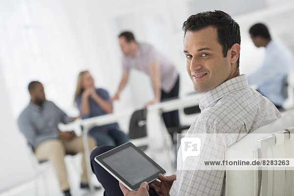Office Interior. Meeting. One Person Looking Over Her Shoulder And Away From The Group. Holding A Digital Tablet.