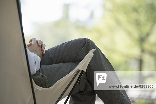Stadtleben. Ein Mann sitzt in einem Segeltuch-Campingstuhl im Park.