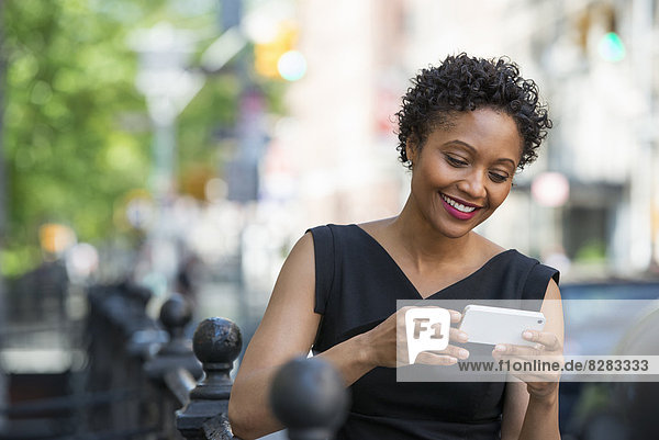 Menschen in Bewegung. Eine Frau in einem schwarzen Kleid in einer Straße der Stadt  die ihr Telefon überprüft.