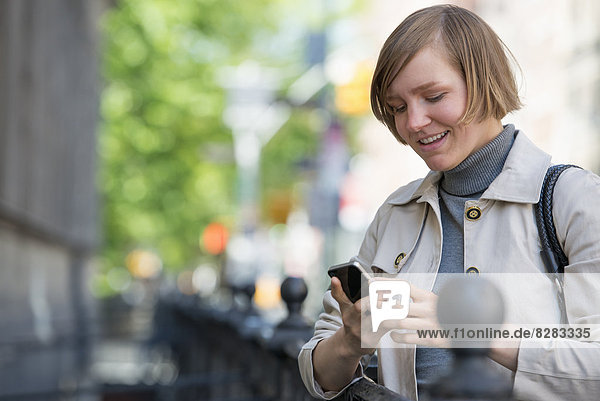 Stadt. Eine Frau in einer Jacke  die ihr Smartphone überprüft.