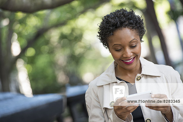 City. A Woman Outdoors In The Park  Checking Her Smart Phone.