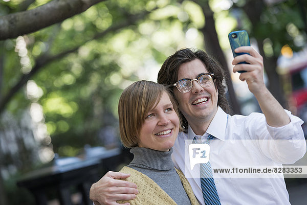 Stadt. Zwei Menschen  ein Mann und eine Frau im Freien  posieren Seite an Seite für ein Foto mit seinem Smartphone.