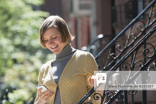 Stadt. Eine Frau auf den Stufen vor einem Stadthaus  um ihr Smartphone zu überprüfen.