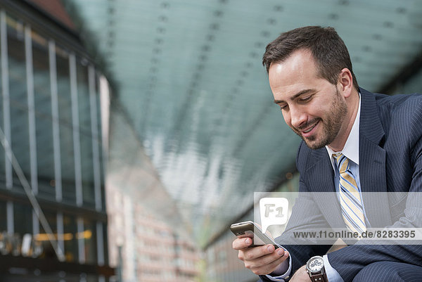 Stadt. Ein Mann im Geschäftsanzug  der seine Nachrichten auf seinem Smartphone abruft.