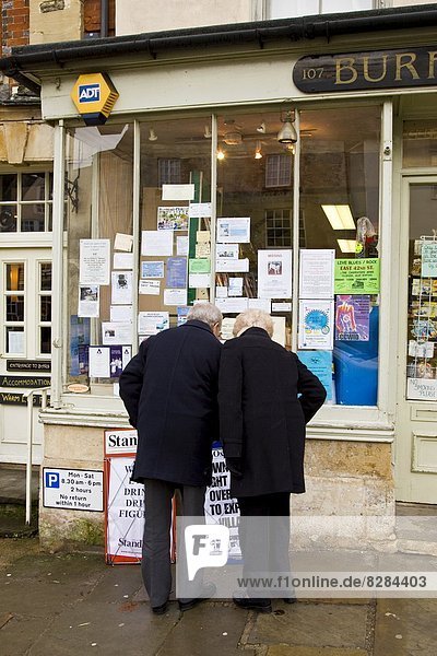 Couple browse the window of a newsagent's shop at Burford in the Cotswolds  United Kingdom