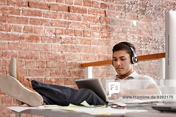 Junger Mann mit digitalem Tablett und Kopfhörer  Füße oben