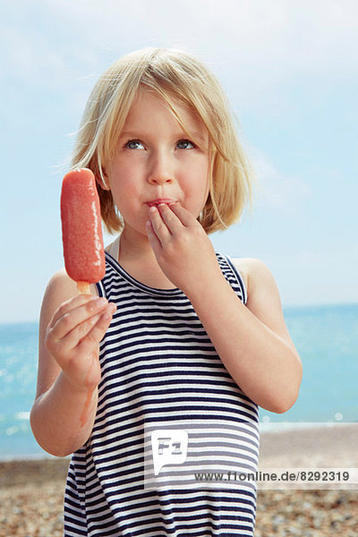 Child with fingers on lip holding ice lolly