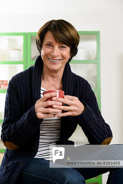 Senior woman sitting on desk holding mug
