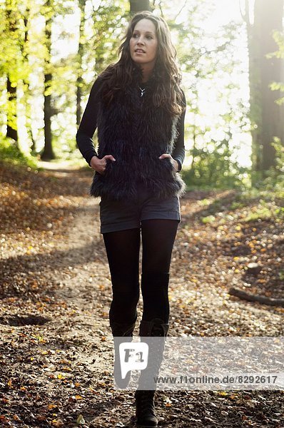 Porträt einer jungen Frau  die im Herbst im Wald spazieren geht.