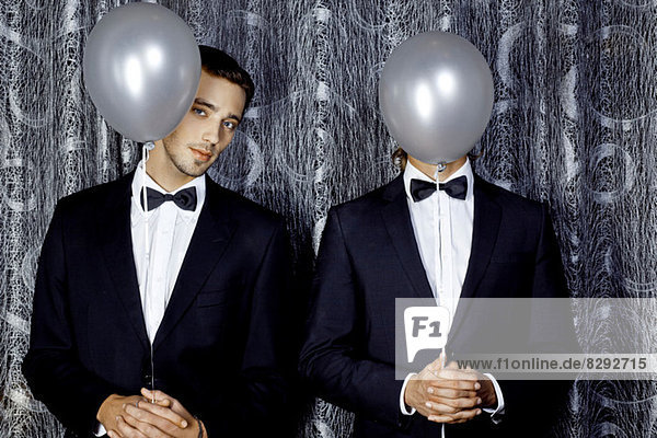 Zwei junge Männer  die sich hinter Luftballons verstecken.