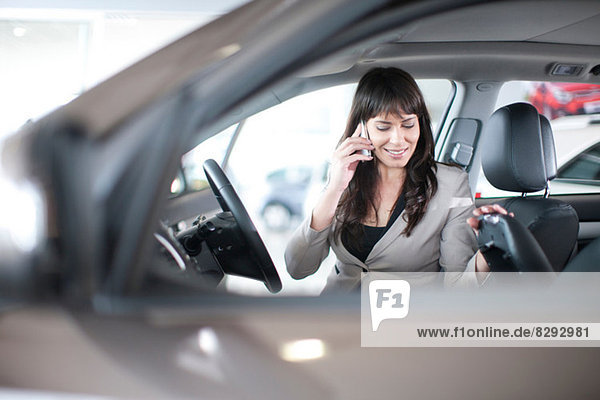 Mid adult woman with mobile phone in car showroom