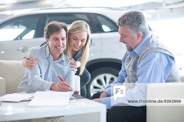 Autoverkäufer und Pärchen unterzeichnen Vertrag im Autohaus