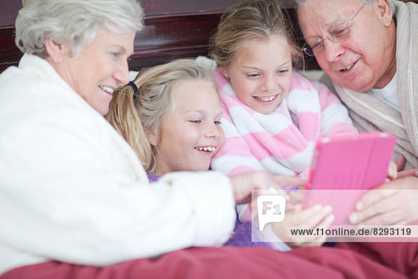 Großeltern und Enkelkinder spielen digitales Spiel im Bett