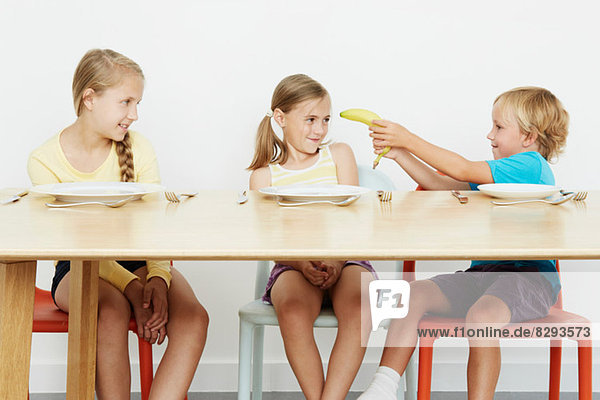 Drei Kinder am Tisch  Junge hält Banane